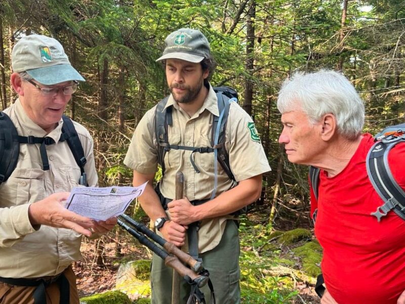 Three men with hiking gear look at a map in a forest.