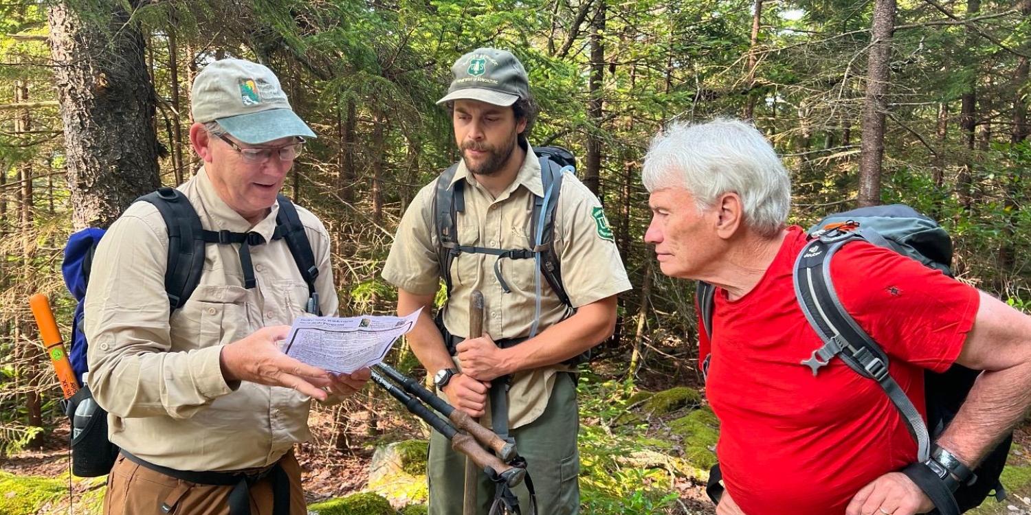 Three men with hiking gear look at a map in a forest.